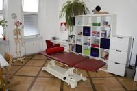 Therapieraum mit einer Werkbank, h&ouml;hen verstellbaren Tisch, einer Liege und allerlei Therapiematerialien.
